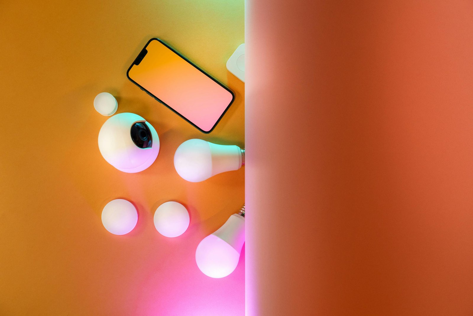 Top view of smart home gadgets including smartphone, camera, and light bulbs in a colorful setup.